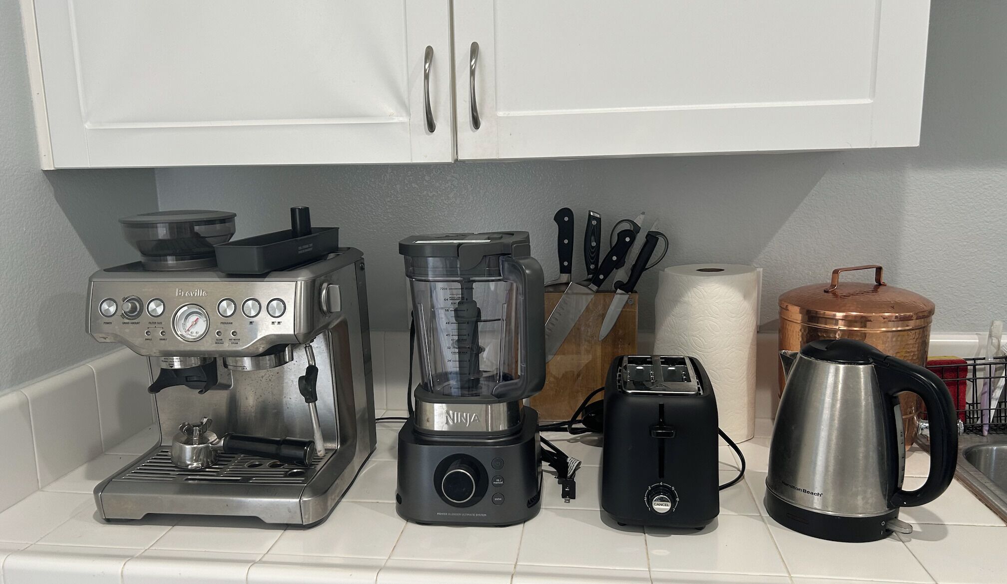 A kitchen with a coffee maker, blender, toaster, kettle, and a copper pot on the counter.