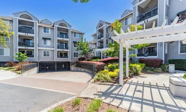 A multi-story residential building with balconies, a covered patio area, and landscaped gardens.