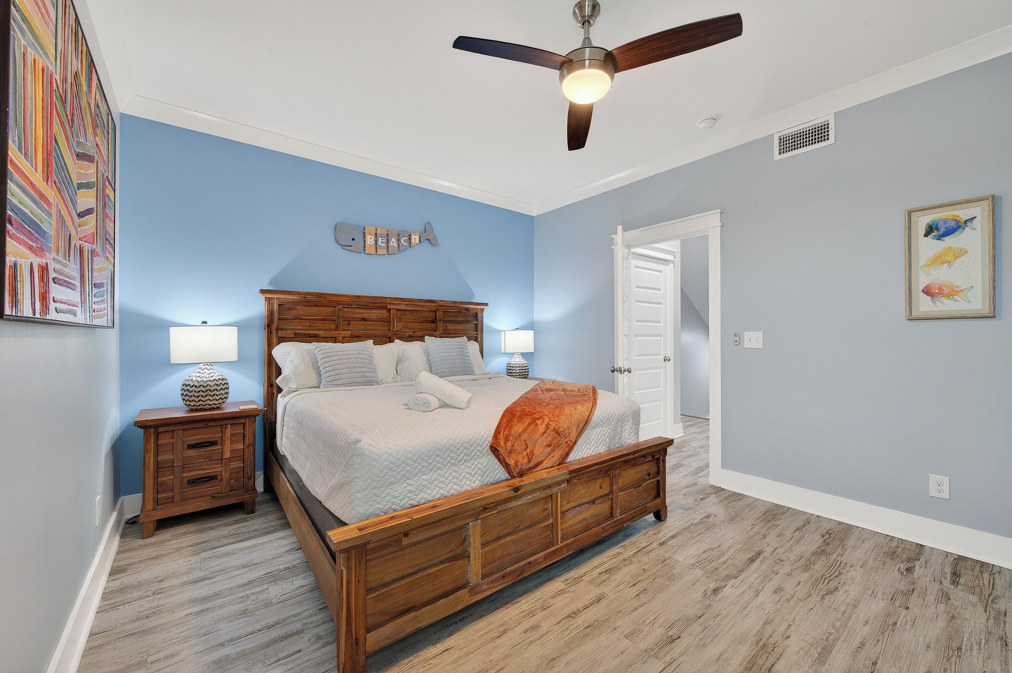 Quarto com cama de madeira, duas mesas de cabeceira, um ventilador de teto e um enfeite de peixe na parede.