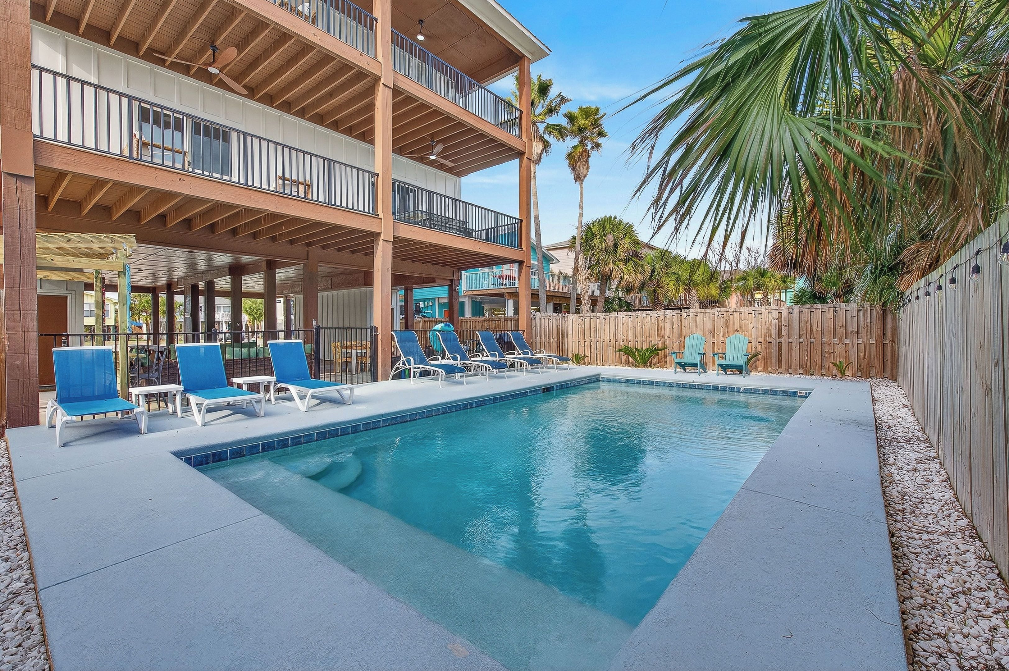 Ein Pool mit Liegestühlen, eine Holzterrasse und ein mehrgeschossiges Gebäude mit Balkonen.