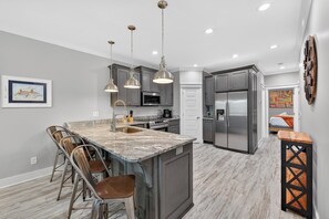 Una cocina moderna con una isla central, iluminación colgante y un refrigerador.
