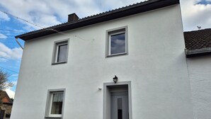 Un edificio blanco con puerta gris, ventanas y una lámpara pequeña sobre la puerta.
