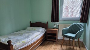 Un dormitorio con cama de madera, mesita de noche, una silla y ventana con cortinas.