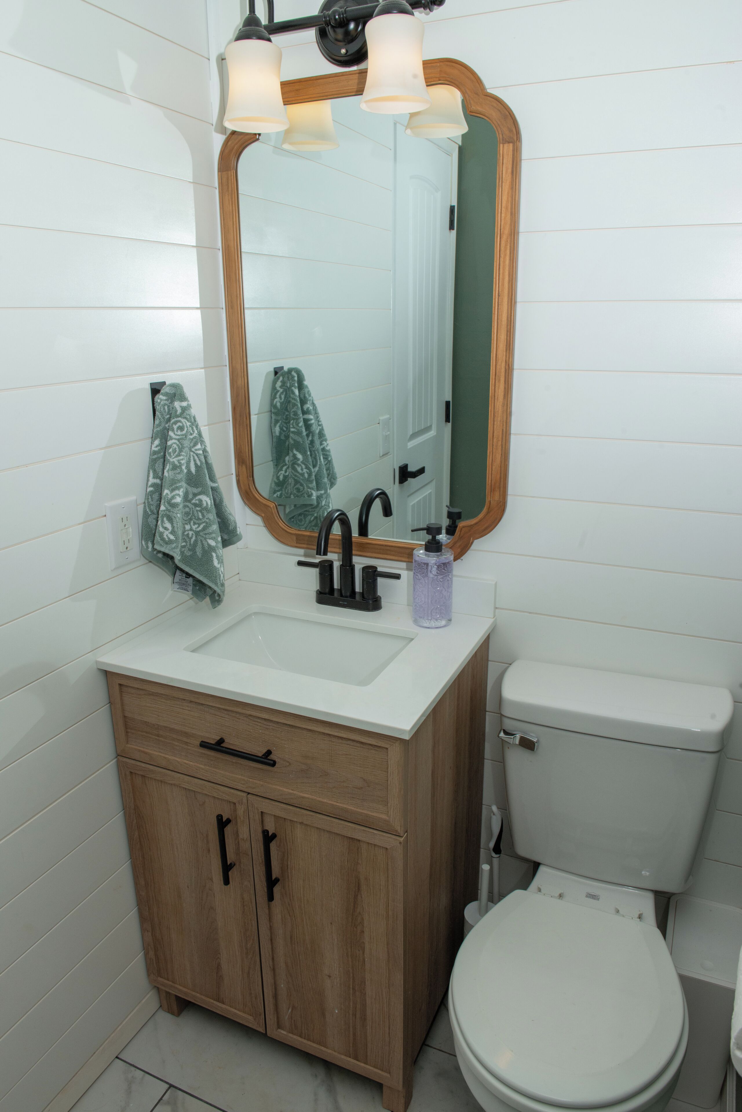 A bathroom with a white sink, wooden vanity, a mirror with a wooden frame, and a white toilet.