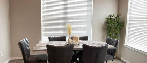 Een eetgedeelte met een ronde tafel, vier stoelen en een bloevas.