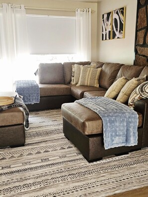 A living room with a brown leather sofa, a patterned rug, and a blue throw blanket. - Enjoyable 4-bedroom house located in Page, AZ, (Page)