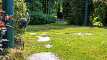 A garden pathway with a bird statue, surrounded by greenery and trees.
