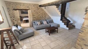 Un salon avec un mur en pierre, un canapé gris, une table basse en bois et un escalier en bois.