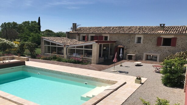 Une piscine, un patio couvert et un bâtiment en pierre avec un toit en tuiles.