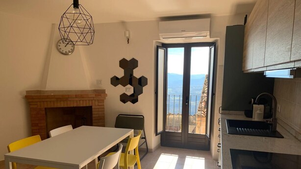 A modern kitchen with a built-in stove, a dining area with a white table and yellow chairs, and a view through a glass door. - Romantic Apartment in an Italian Village near Pollino National Park (Castelluccio Superiore)