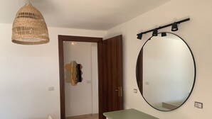 A bedroom with a bed, a green table, a mirror, a hanging light fixture, and a door leading to another room. - Romantic Apartment in an Italian Village near Pollino National Park (Castelluccio Superiore)