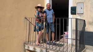 A man and a woman standing on a balcony with a metal railing, a door, and a mailbox on the building's facade. - Romantic Apartment in an Italian Village near Pollino National Park (Castelluccio Superiore)
