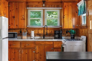 Una cocina con armarios de madera, un lavamanos doble, una estufa y un microondas.