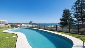 A curved swimming pool with a clear view of the sea and buildings in the background. - Sundeck Shoal Bay Ground floor with views and pool access (Shoal Bay)