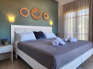 A neatly made bed with pillows, a bedside table with a lamp, and decorative wall mirrors. - Matthew's Place (Malia)