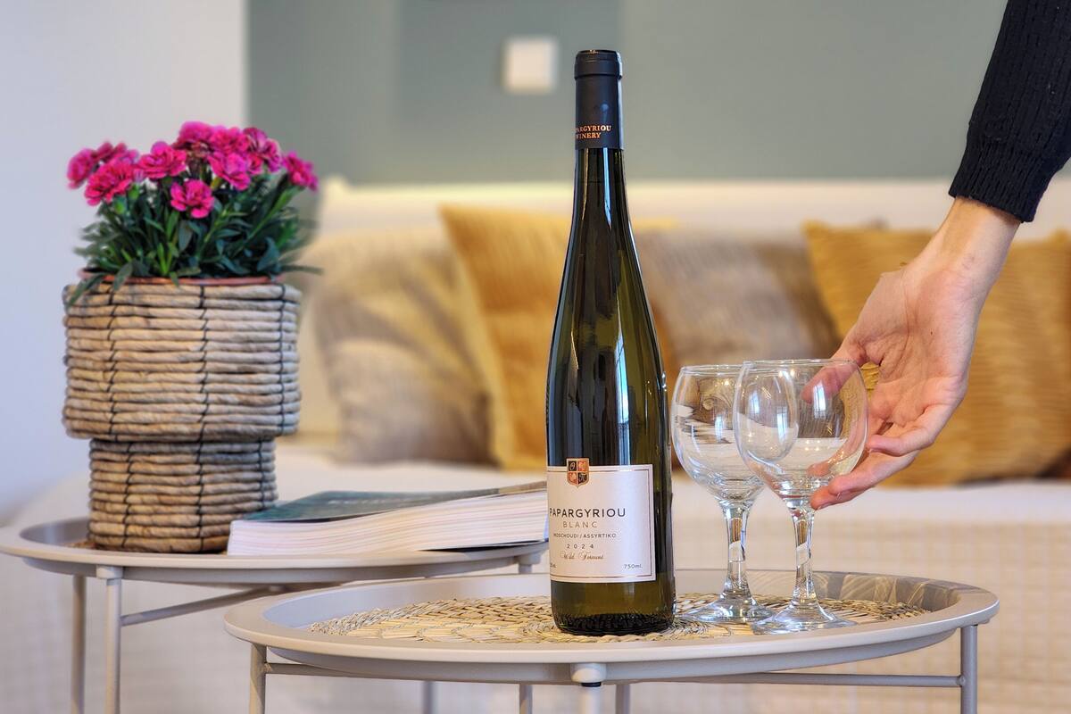 A bottle of wine on a tray with two glasses, a woven basket with flowers, and a sofa in the background.