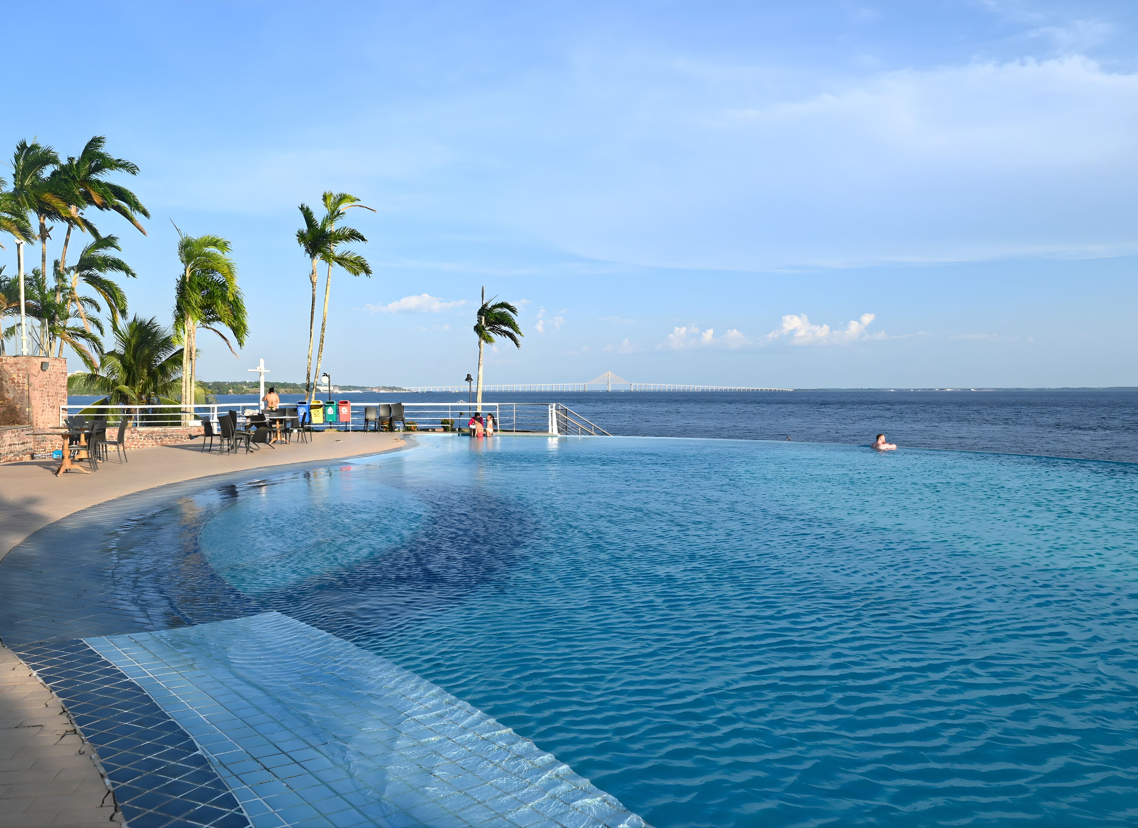 A poolside area with a view of the ocean and a bridge in the distance.