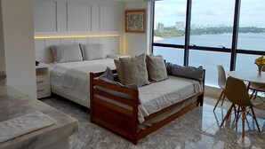 Camera moderna con letto, divano, angolo pranzo e vista sul mare.