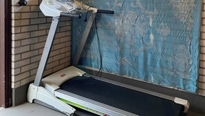 A treadmill in a room with brick walls, a window, and a blue curtain.
