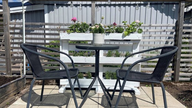 A patio with two chairs and a table, a wooden fence, and a planter with flowers.