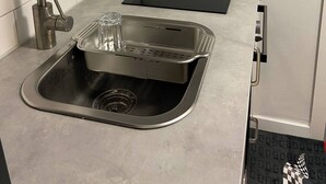 A modern kitchen with a stainless steel sink, a faucet, a black countertop, and a stainless steel range hood.