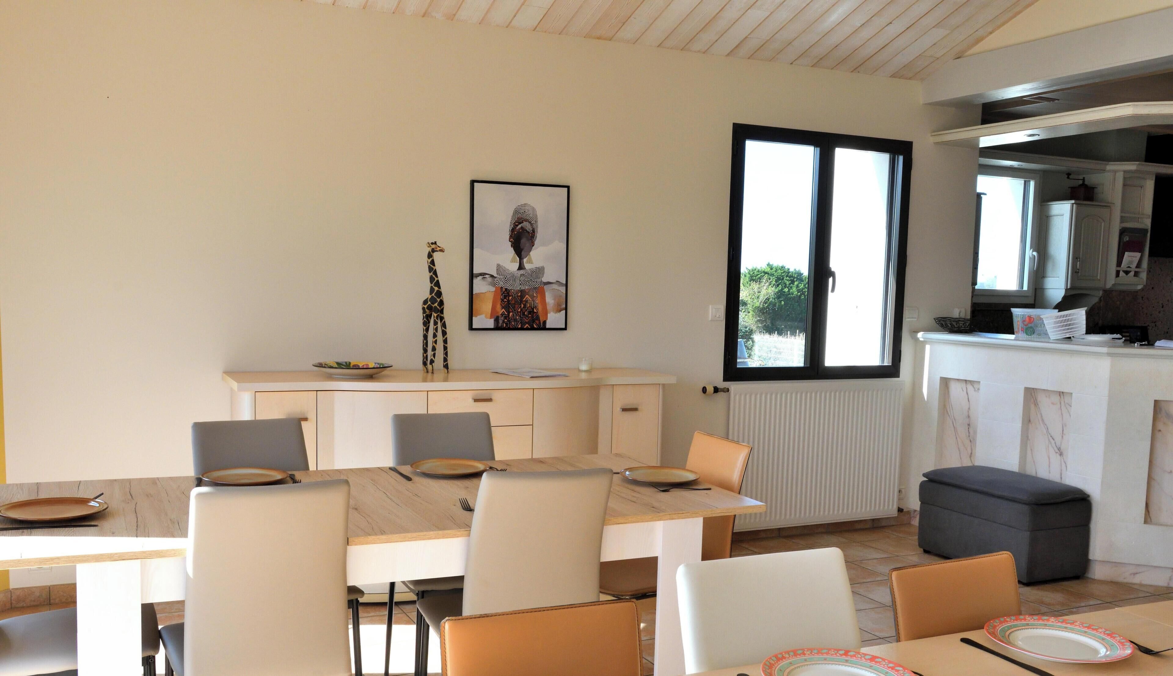 A dining area with a table and chairs, a kitchen with a window, and a framed picture on the wall.
