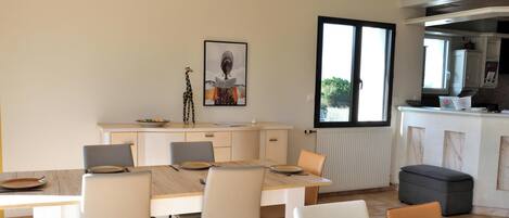 A dining area with a table and chairs, a kitchen with a window, and a framed picture on the wall.