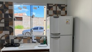 A kitchenette with a refrigerator, a sink, and a window with a view of a car and buildings.