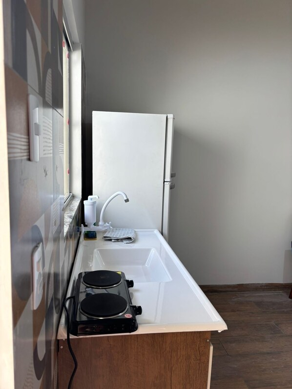 A compact kitchenette with a white refrigerator, a sink, and a small stove.