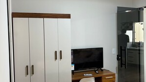 A bedroom with a bed, a desk with a TV, a wardrobe, and a glass door leading to a bathroom.