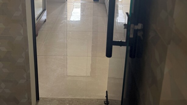 A corridor leading to a dining area with chairs and a table, a tiled floor, and a door on the left.