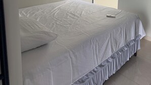 A bedroom with a bed, an air conditioning unit, and a door leading to another room.