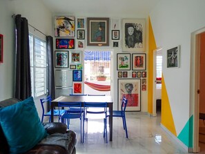 Ein Essbereich mit Tisch und Stühlen, ein Sofa mit Kissen und eine Küche im Hintergrund.