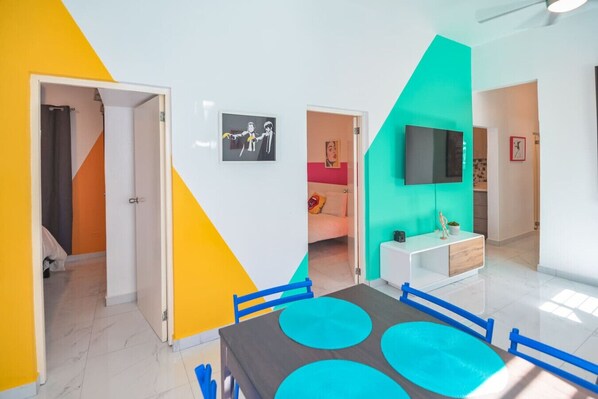 Ein modernes Zimmer mit Essbereich, einem an der Wand befestigten Fernseher und einer Tür zu einem weiteren Raum.