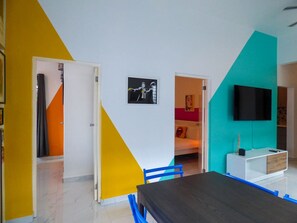Ein modernes Zimmer mit einem großen Tisch, einem Fernseher und einem farbenfrohen Wanddesign.