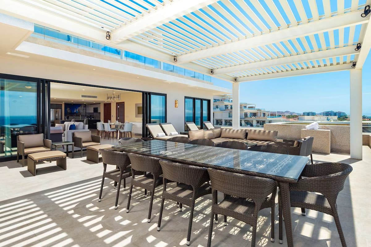 A rooftop terrace with a glass table, wicker furniture, and a view of the city.