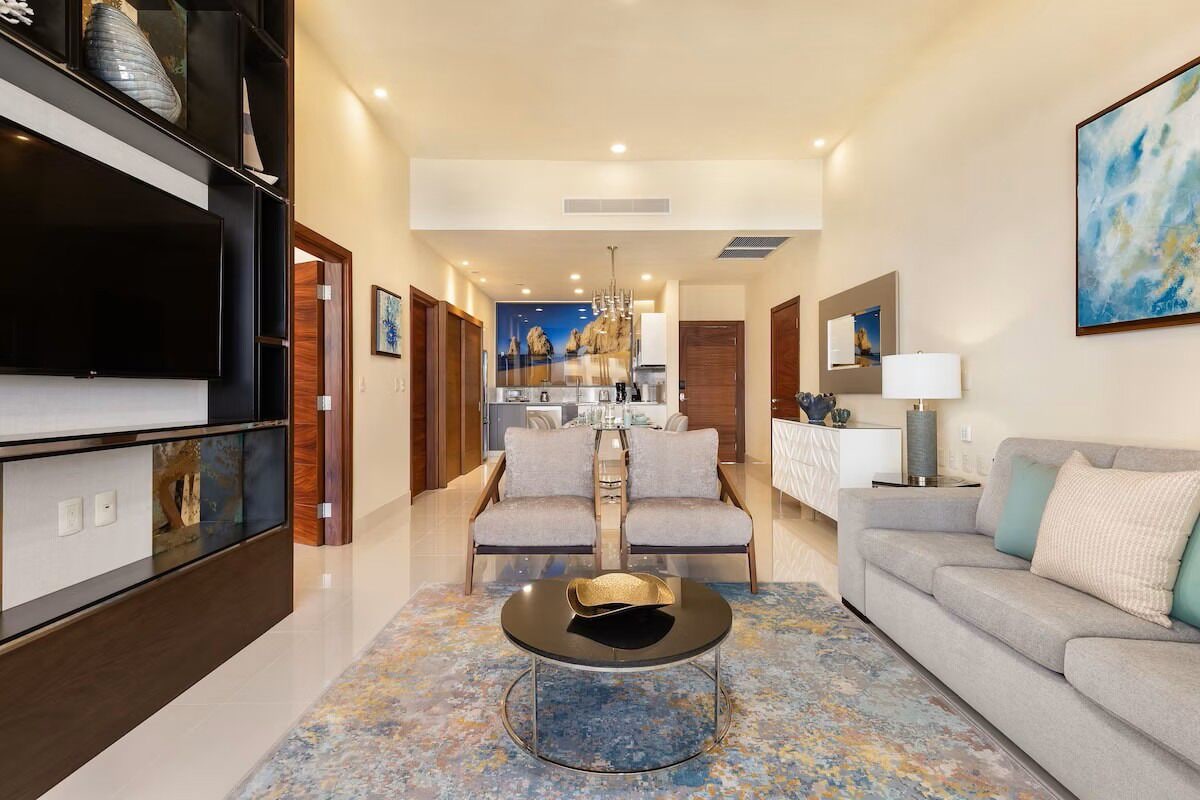 A modern living room with a flat-screen TV, a round coffee table, two sofas, and a kitchen in the background.