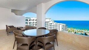 A balcony with wicker furniture, a glass table, and a view of the ocean and hotel buildings. - Villa La Valencia (San José del Cabo)