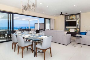 A modern living room with a glass dining table, grey sofa, and a TV mounted on the wall. - Villa La Valencia (San José del Cabo)