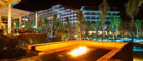 A hotel with a pool area, palm trees, and a night-time illuminated setting.