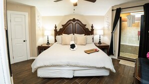 Un dormitorio con una cama grande, un ventilador de techo, dos mesitas de noche con lámparas, una puerta y vistas al exterior.