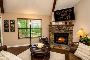 A cozy living room with a stone fireplace, a leather ottoman with candles, and a sign reading 'Bootlegger's Villa.' - Bootleggers Villa | Hot Tub • Mtn Views • Pet (Gatlinburg)