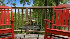 Una terraza de madera con sillas rojas y una mesita con dos vasos de cerveza.