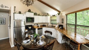 Una cocina con armarios blancos, un refrigerador de acero inoxidable, un microondas y un comedor con una mesa dispuesta para dos personas.