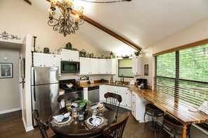 Una cocina con armarios blancos, un refrigerador de acero inoxidable, un microondas y un comedor con una mesa dispuesta para dos personas.