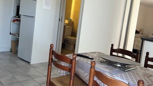 A room with a bed, wooden chairs, a small kitchenette with a microwave and refrigerator, and a bathroom visible through an open door. - Relaxing under the olive trees (Santa-Reparata-di-Balagna)