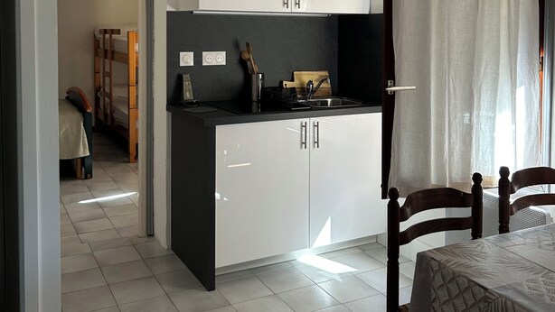 A compact kitchen with white cabinets, a black countertop, and a dining area with a table and chairs. - Relaxing under the olive trees (Santa-Reparata-di-Balagna)
