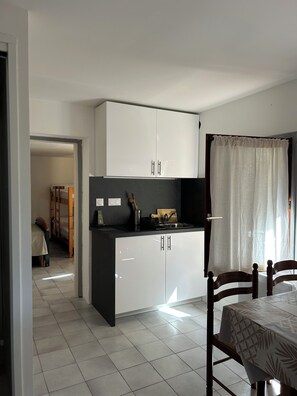 Una cocina compacta con armarios blancos, encimera negra y comedor con mesa y sillas.
