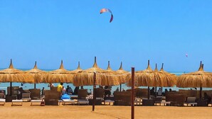 Una playa con sombrillas de paja y sillas de descanso.
