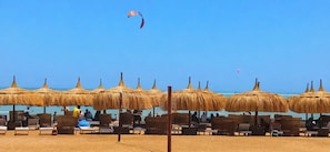 A beach with thatched umbrellas and lounge chairs. - Relax Stays Fanadir Bay Hurghada (Hurghada)